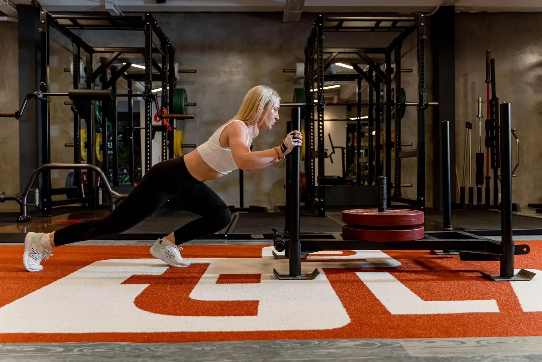 A gym member pushing a heavy sled across turf, demonstrating the physical routine of gym member engagement.